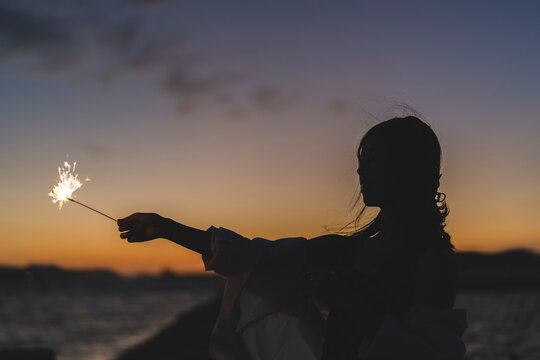 夕暮れの海で花火をする女性