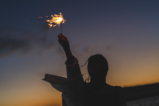 夕暮れの海で花火をする女性