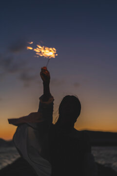 夕暮れの海で花火をする女性