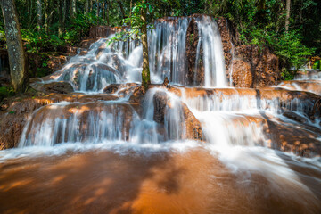 Naklejka premium Silky smooth water flow cascading over brown limestone rock tiers at Pa Wai Waterfall in green tropical forest, Phop Phra District, Tak Province, Thailand. Beautiful natural jungle landscape view.