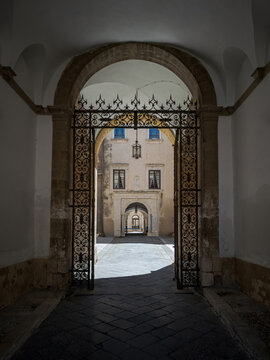 Traditional stone gateway featuring historic ironwork and flagstone pavement in Siracusa, Italy. Scenic architectural perspective of an old town mansion entry hall.