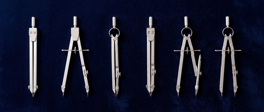 Selection of professional silver metal drawing compasses and engineering tools displayed on dark blue velvet background for technical design and geometry work.