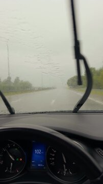 Rainy highway view from car interior with blurred windshield, dashboard speedometer showing 100 kmh