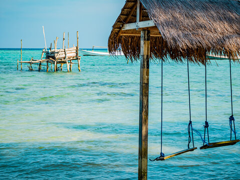 Wooden swings hanging from a thatched roof enjoying the clear blue green ocean water on Barakuda Beach. Creating a relaxing scene highlighting tropical travel and serene island life in Karimunjawa