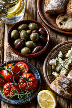 Flat lay shot of a rustic wooden table filled with Mediterranean dishes: green and Kalamata olives, tomatoes with olive oil, feta cheese and bread.