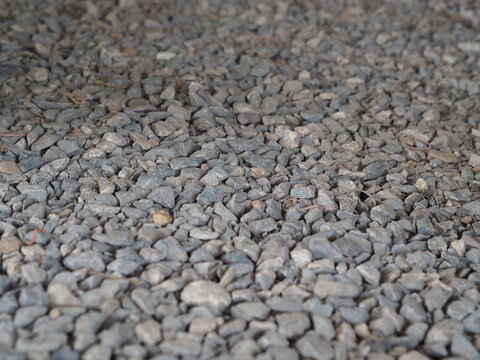 detailed, natural light photograph showcasing the rough and varied texture of a ground surface covered in gray crushed aggregate gravel and small pebbles. The image presents a realistic depiction of a
