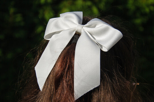 Schoolgirl prepares for the school year with a white hair bow on her head. The scene is outdoors in a green area