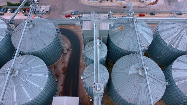 Aerial view of steel silo roofs and trusses. Metal roofs and elevator structures stand beside an asphalt road with parked vehicles.