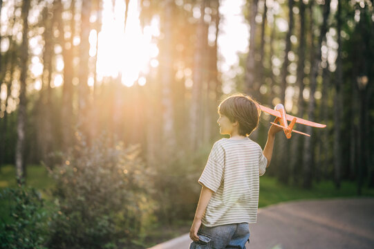 Boy walks in the park at sunset launching a toy airplane