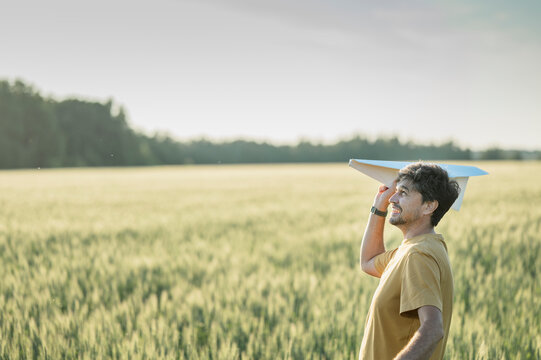 Smiling man launches a paper airplane in a summer field at sunset