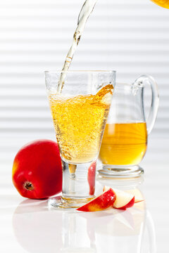 Carafe and glass with pouring apple juice, close up