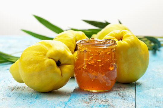 Four quinces (Cydonia oblonga), a spoon and a glass of quince marmalade on wooden table