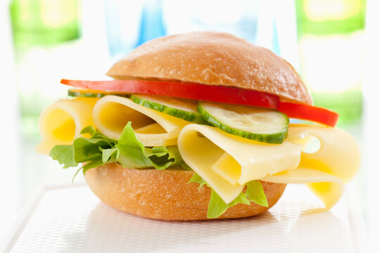 Bread roll with Emmentaler cheese, cucumber and peppers on chopping board, close up