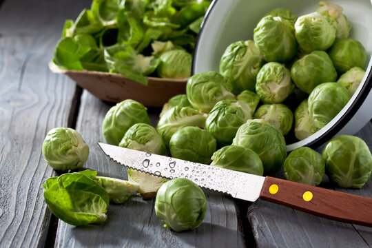 Bowl of Brussels sprouts, plate with peels and kitchen knife on grey wooden table