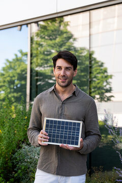Smiling man holds a solar panel outdoors for clean energy