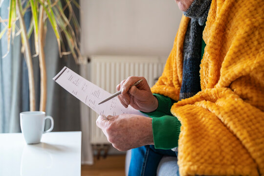 Person reviewing heating bill at home wrapped in blanket and scarf