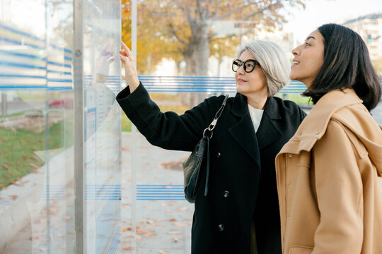 Mother and daughter read a bus schedule at the station