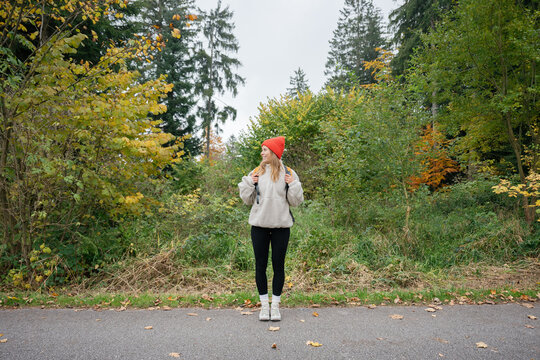 A happy woman with a backpack stands on a forest road in autumn