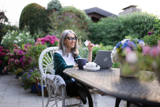 Freelance woman uses credit card on laptop in garden