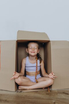 Child sitting cross legged in cardboard box meditating during moving