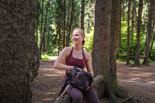 A smiling woman rests on a log in the forest after a workout