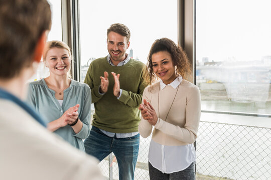 Three smiling colleagues applauding for mature woman in office