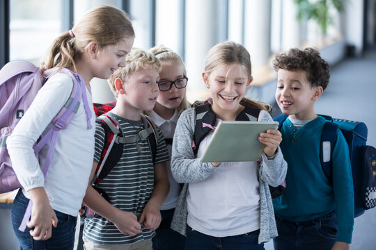 Excited students gather around a tablet in the school hallway, eager to learn and explore new technology