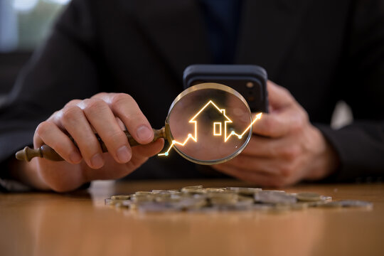 Businessperson using smartphone with magnifying glass over coins, house icon rising arrows, representing real estate investment, property market growth finance mortgage home valuation.