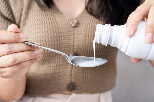Close-up of woman pouring liquid antacid medicine from white bottle into spoon. Ideal for heartburn relief, GERD treatment, stomach ache, indigestion, and healthcare