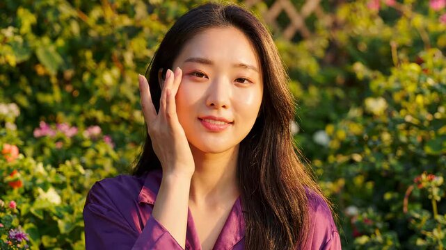 Beautiful young woman touching glowing facial skin outdoor sunny garden portrait asian female model routine skincare wellness concept healthy complexion makeup beauty spa