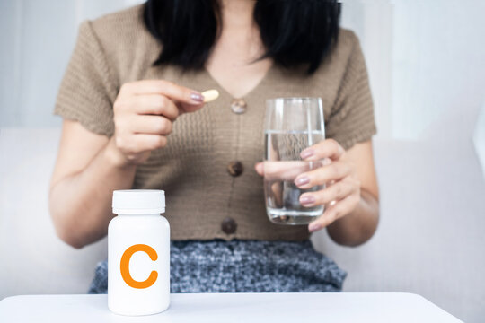 Asian woman taking vitamin C pill with glass of water and white supplement bottle. Ideal for immune booster, healthcare, dietary supplement, skin care, and wellness 