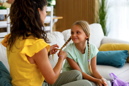 Mother gently braiding her young daughter&rsquo;s hair while they spend quality time together at home