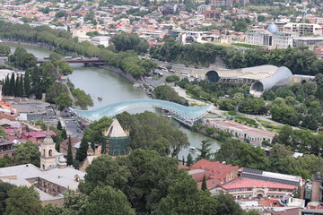 Aerial view of Tbilisi, Georgia with Peace Bridge over Kura river, old town rooftops, church towers and Rike park among lush greenery. © Ольга Дербасова