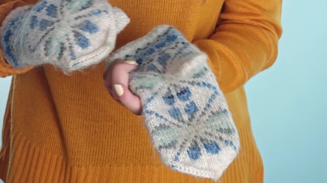Hands show knitted gloves with blue and white patterns in a warm room