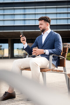 Businessman checking smartphone during coffee break outside office