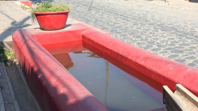 Pila de las Culebras traditional red public water fountain beside a cobblestone street in Tapalpa Pueblo M&aacute;gico, Jalisco, Mexico. Cultural landmark static shot.
