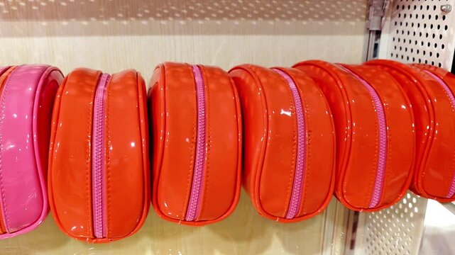 Pink and orange glossy handbags displayed in a row on a retail store shelf. Colorful fashion accessories with zipper closures arranged neatly for sale in a modern shop.
