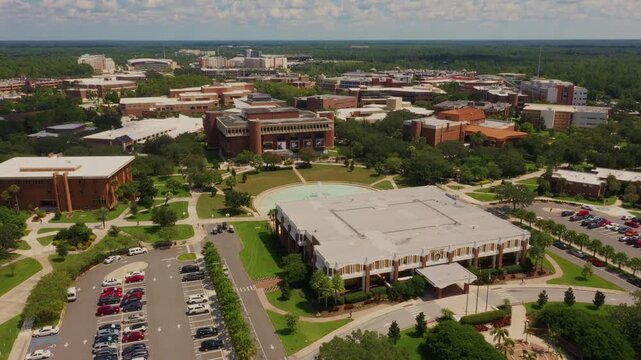 High-altitude drone view of the University of Central Florida campus, featuring Millican Hall, the iconic Reflecting Pond, and the John C. Hitt Library beyond.