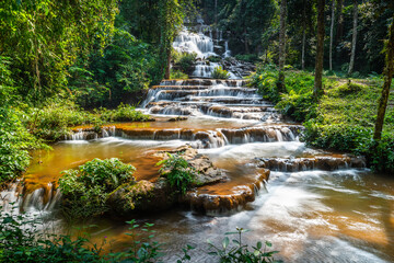 Fototapeta premium Beautiful multi-tiered Pha Charoen Waterfall cascading through lush green tropical rainforest in Namtok Pha Charoen National Park, Phop Phra District, Tak Province, Thailand.