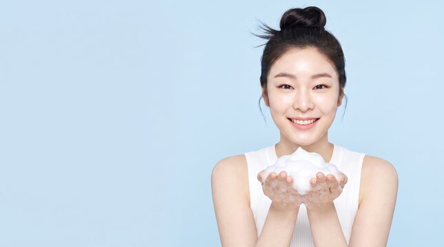 Smiling Asian woman holding fluffy cleansing foam in open palms in blue studio