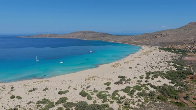 Experience the stunning landscapes of Simos Beach in Elafonisos, Greece. White sands meet turquoise waters as sailboats glide gently, creating a serene vacation atmosphere in paradise.