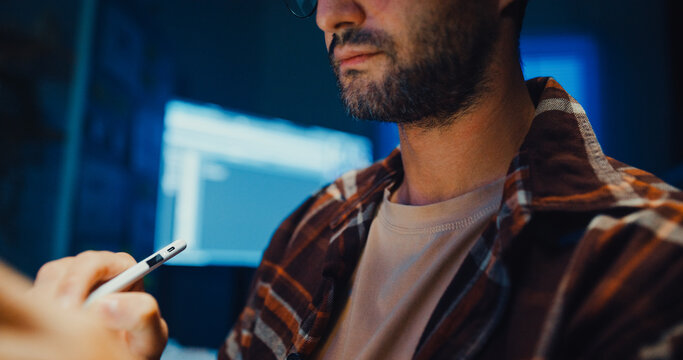 Young Caucasian male programmer use tablet for code design and plan in dark home office at night. AI technology, cybersecurity, software developer, freelance innovation, digital data network concept.