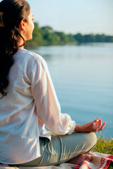 Naklejka premium Vertical image of young adult Asian woman practicing yoga and meditating by river. Scene represents mental wellbeing and mindfulness, perfect for wellness and health campaign