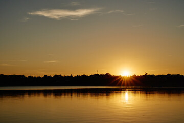 Naklejka premium Golden sunset over calm lake with sun reflection