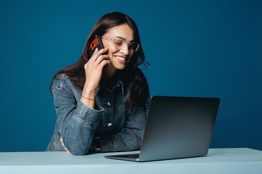 A woman handles work while talking on her smartphone on a blue background setup