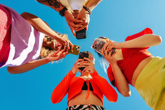 Group of young friends absorbed in smartphones under clear blue sky