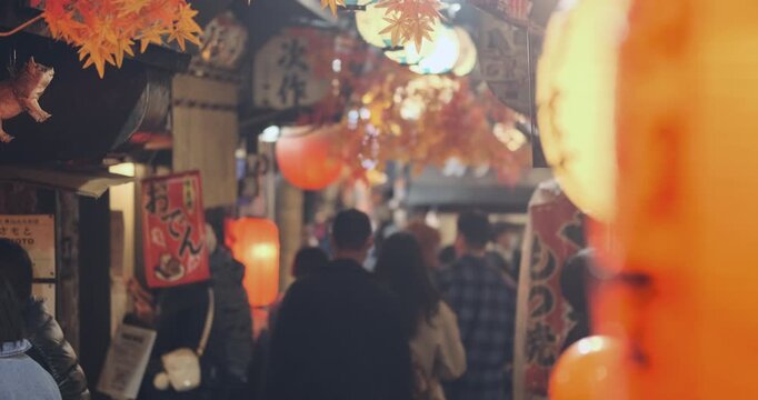 Omoide Yokocho authentic Japan shopping street at night. Asia downtown culture in Tokyo. People walking through narrow traditional japanese alley illuminated by glowing orange lanterns in evening