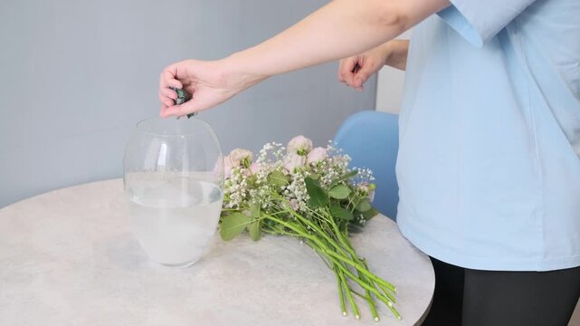 woman adds crushed aspirin to water in glass vase to preserve fresh bouquet. adding aspirin to water helps keep bouquet alive longer. bouquet care with aspirin extends vase life of flowers