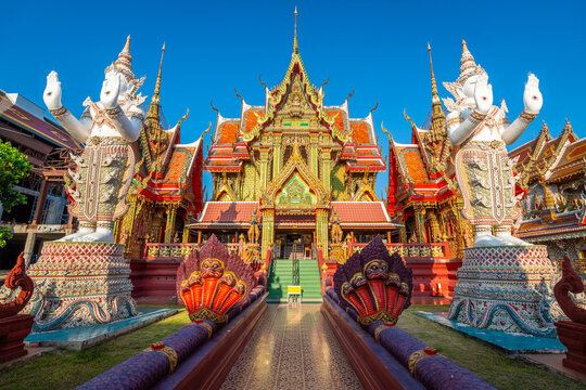 Stunning view of the golden main hall of Wat Si Uthumphon with giant white statues in Nakhon Sawan. The vibrant red and gold temple architecture is framed by multi-headed serpent sculptures.