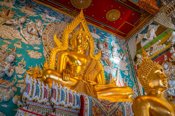 Fototapeta premium Golden Buddha statue inside the hall of Wat Sri Uthumphon in Mueang Nakhon Sawan District, Nakhon Sawan, Thailand, surrounded by ornate white relief wall art and celestial angels.
